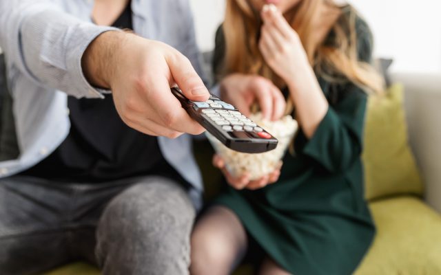 Paar diivanil, üks hoiab kaugjuhtimispulti, teine sööb popkorni